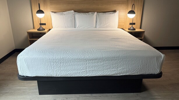 Una cama grande con cabecera de madera, dos mesitas de noche con lámparas y un suelo de tono claro.