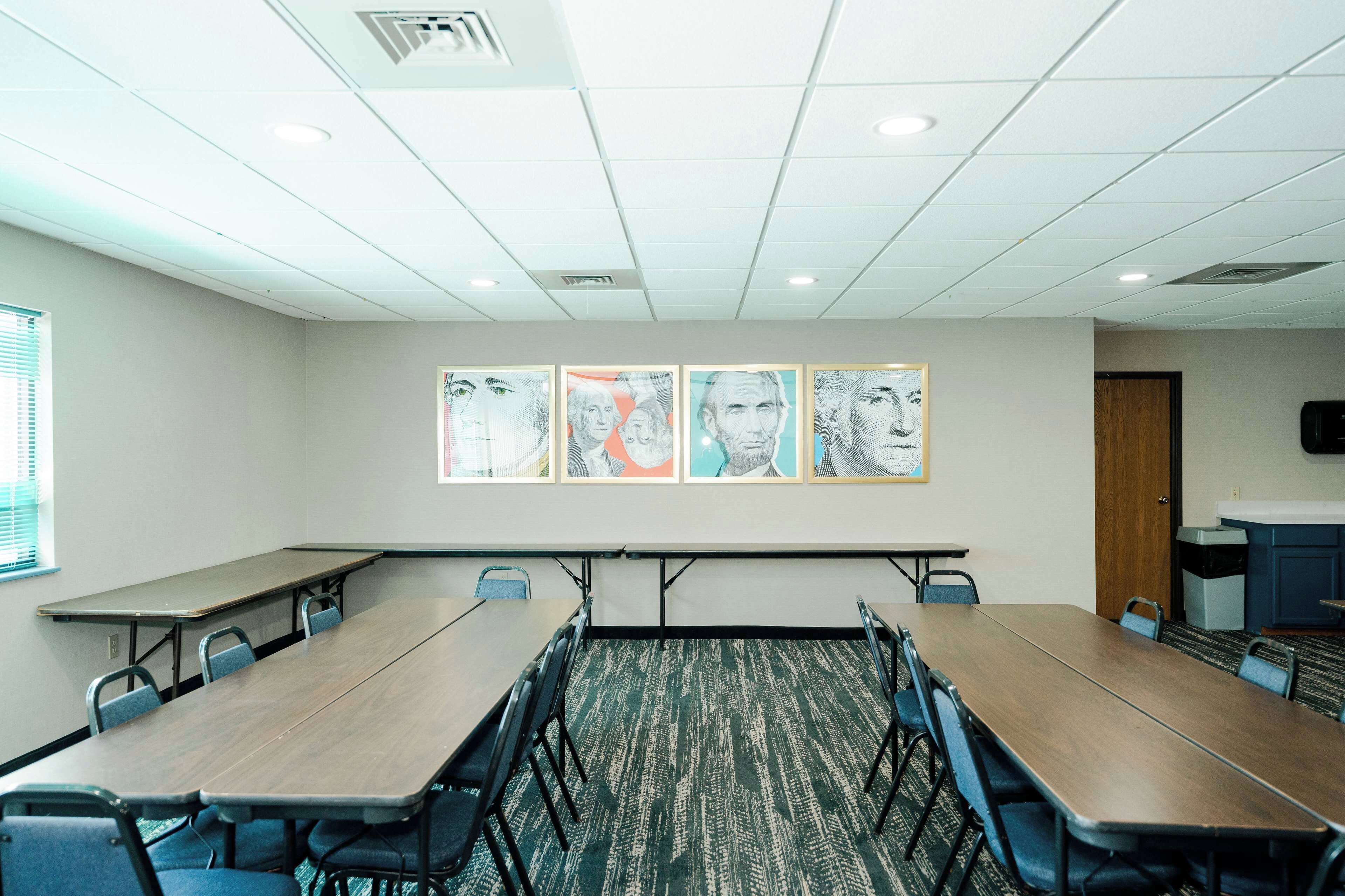 A conference room with a long table, chairs, and a carpeted floor. There are ceiling lights and a door in the background.