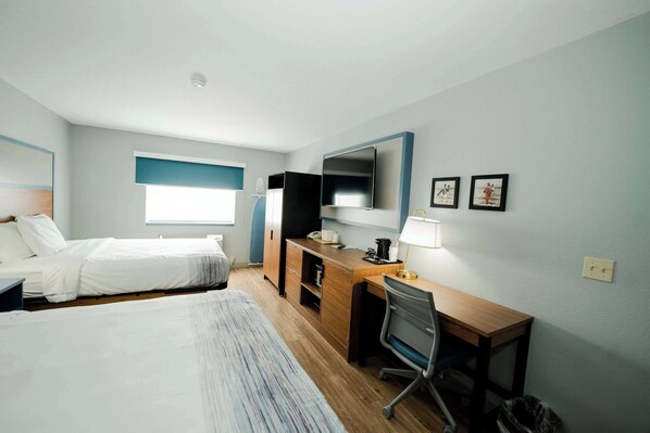Habitación de hotel con dos camas, un escritorio, una silla, un televisor y un ventanal pequeño.