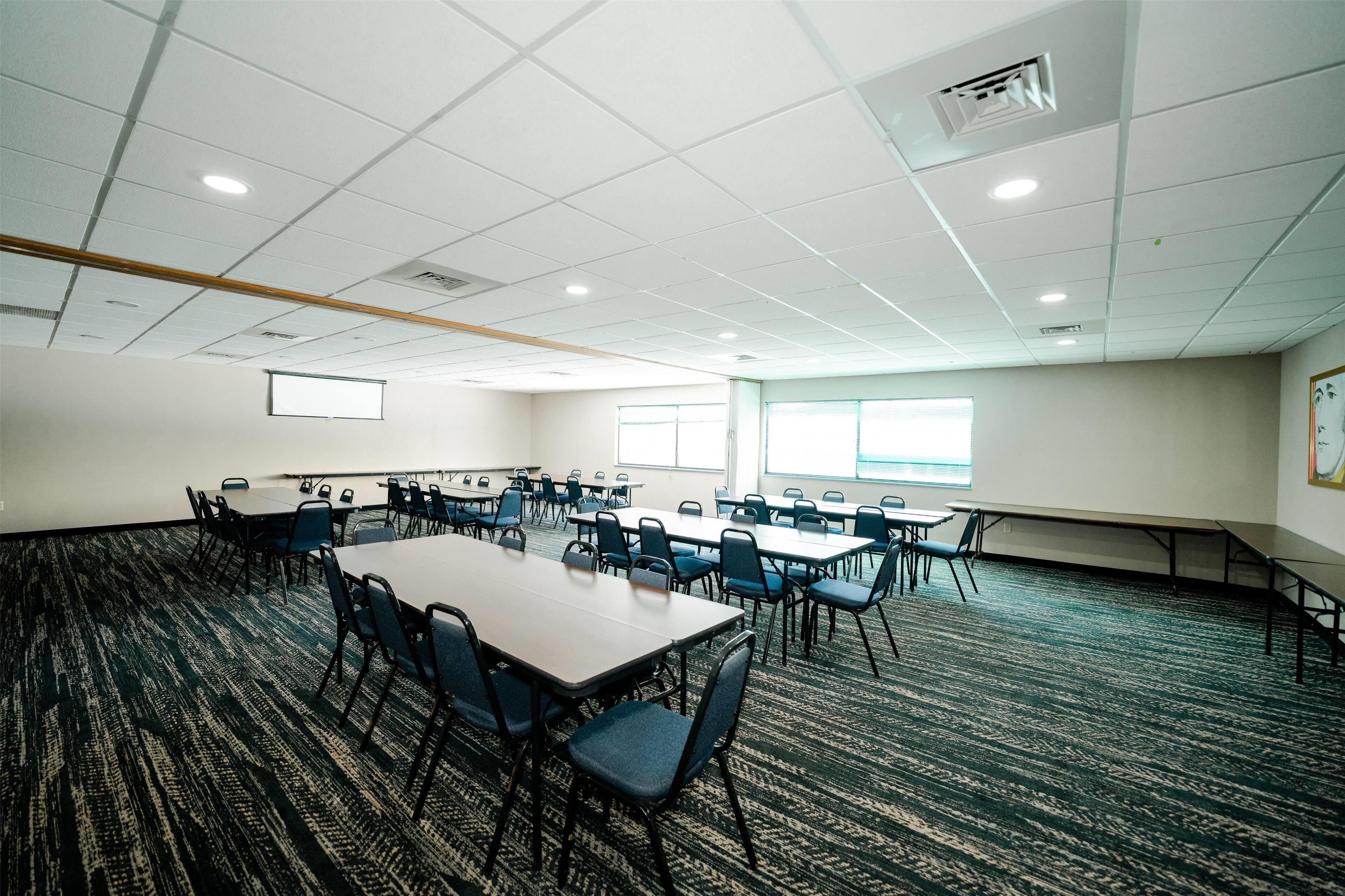 A conference room with multiple tables and chairs, carpeted flooring, and large windows.