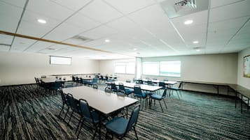 A conference room with multiple tables and chairs, carpeted flooring, and large windows.