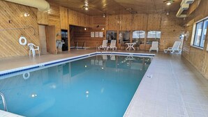 Una piscina interior con suelo de baldosas, paredes de madera y sillones reclinables blancos.