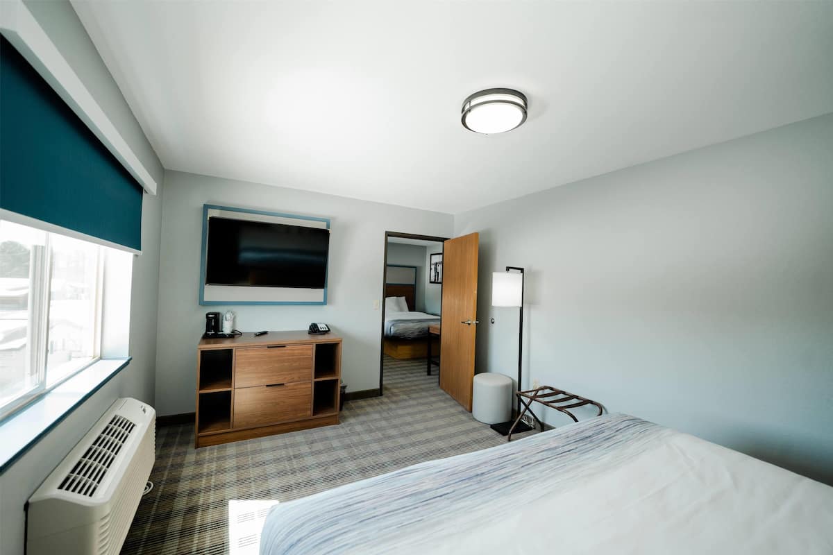 A modern hotel room with a bed, a desk, a wardrobe, a TV, and a window with blinds.