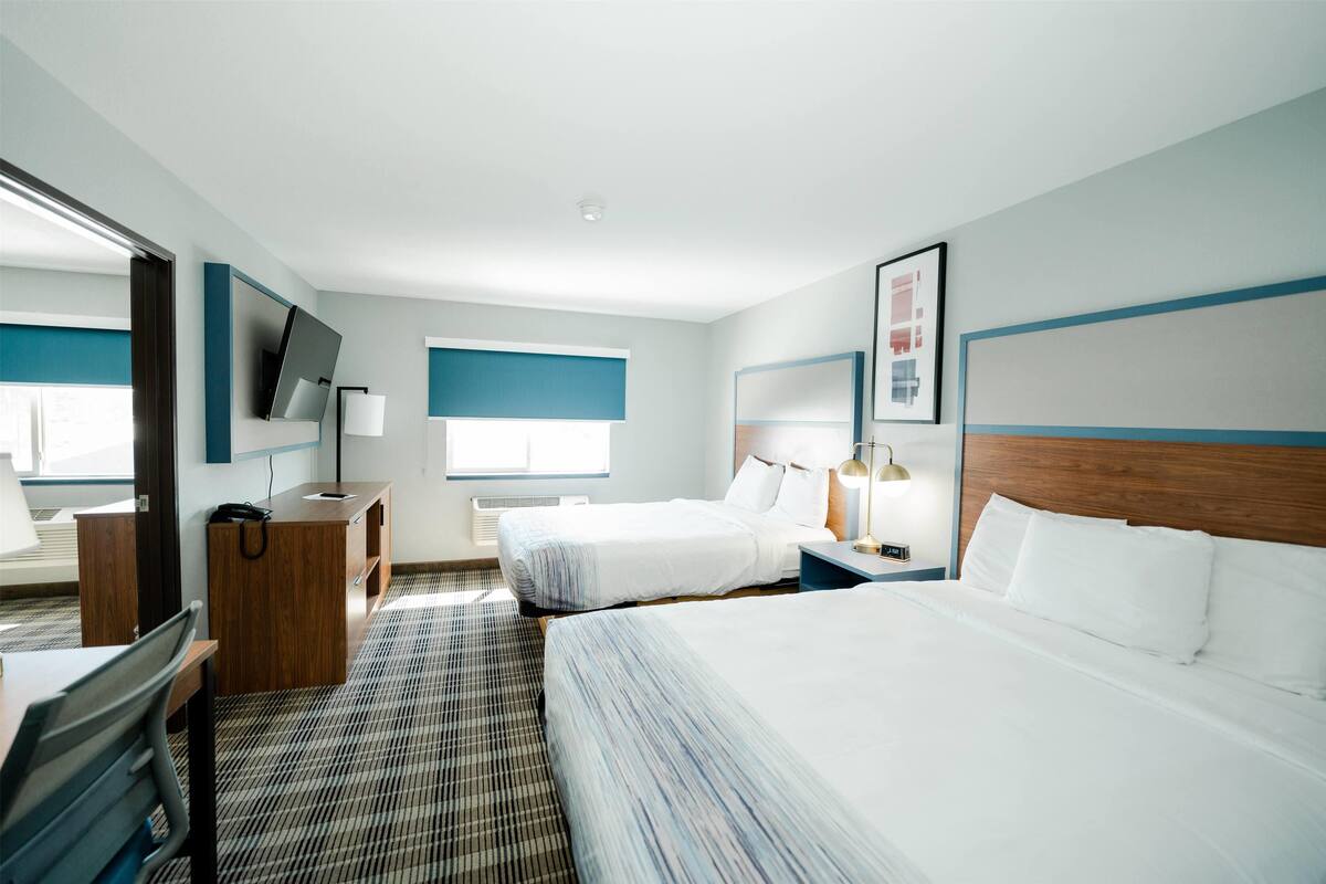 A hotel room with two beds, a desk, a TV, and a window.