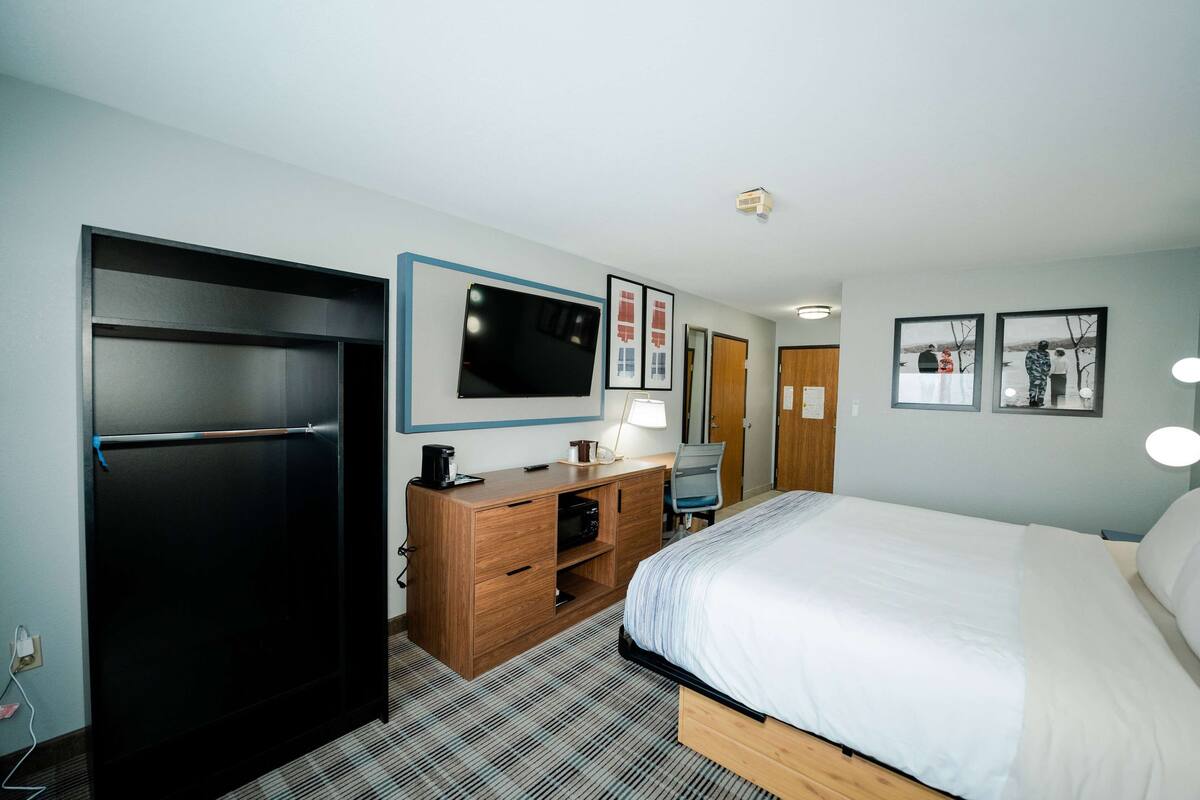 A hotel room with a bed, a desk with a lamp, a television, and a wardrobe.