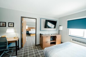 Habitación de hotel con cama, escritorio, silla, televisor y baño visible a través de una puerta abierta.