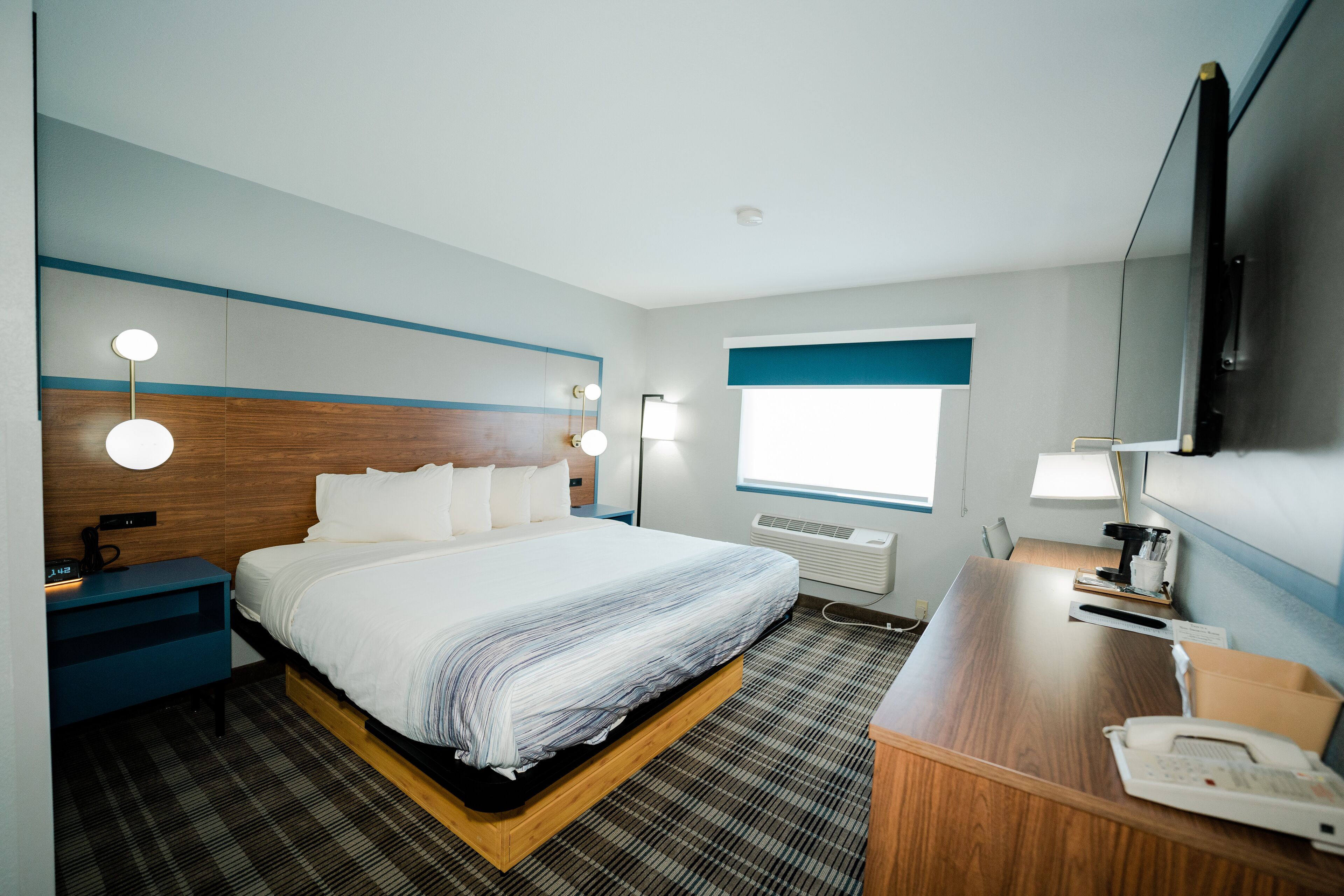 Een hotelkamer met een bed, nachtkastje, lamp en bureau met telefoon.