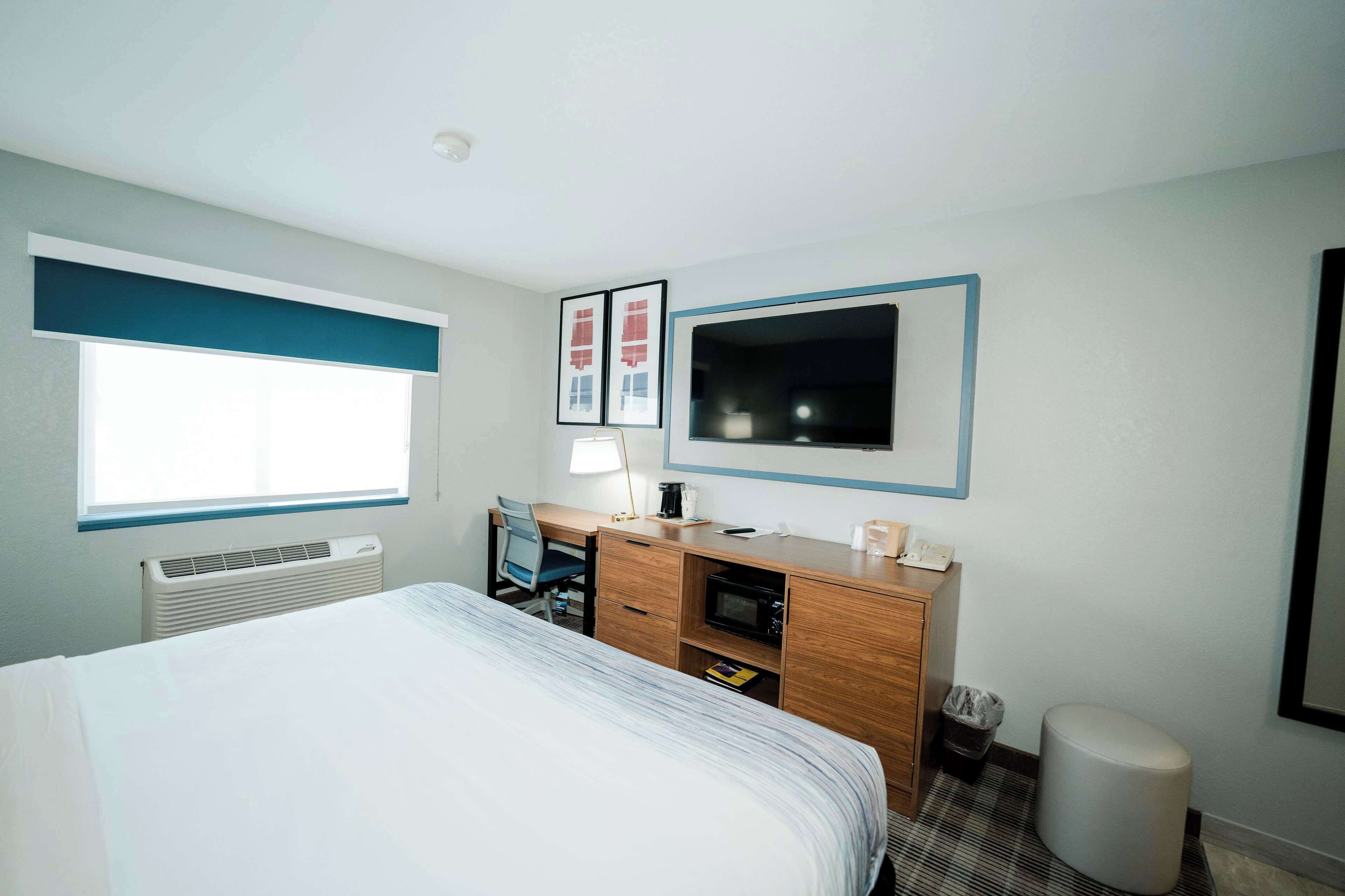 A hotel room with a bed, a desk, a TV, and a window.