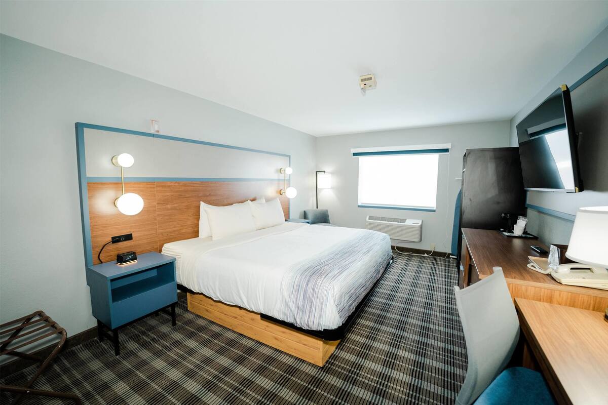 A hotel room with a bed, bedside table, lamp, desk, chair, and a television.