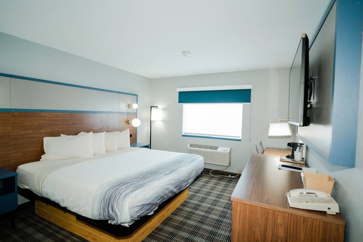 A hotel room with a bed, bedside table, desk, lamp, phone, and a TV.