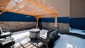Un patio techado al aire libre con una pérgola de madera, asientos y un barril.