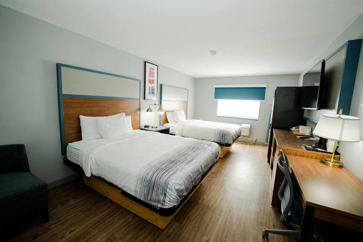 A hotel room with two beds, a desk with a lamp, a TV, and a window.
