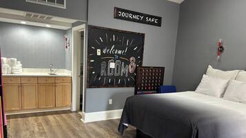 Habitación de hotel con cama, un pequeño escritorio, una kitchenette y un cartel que dice 'WELCOME TO ROOM 8'.