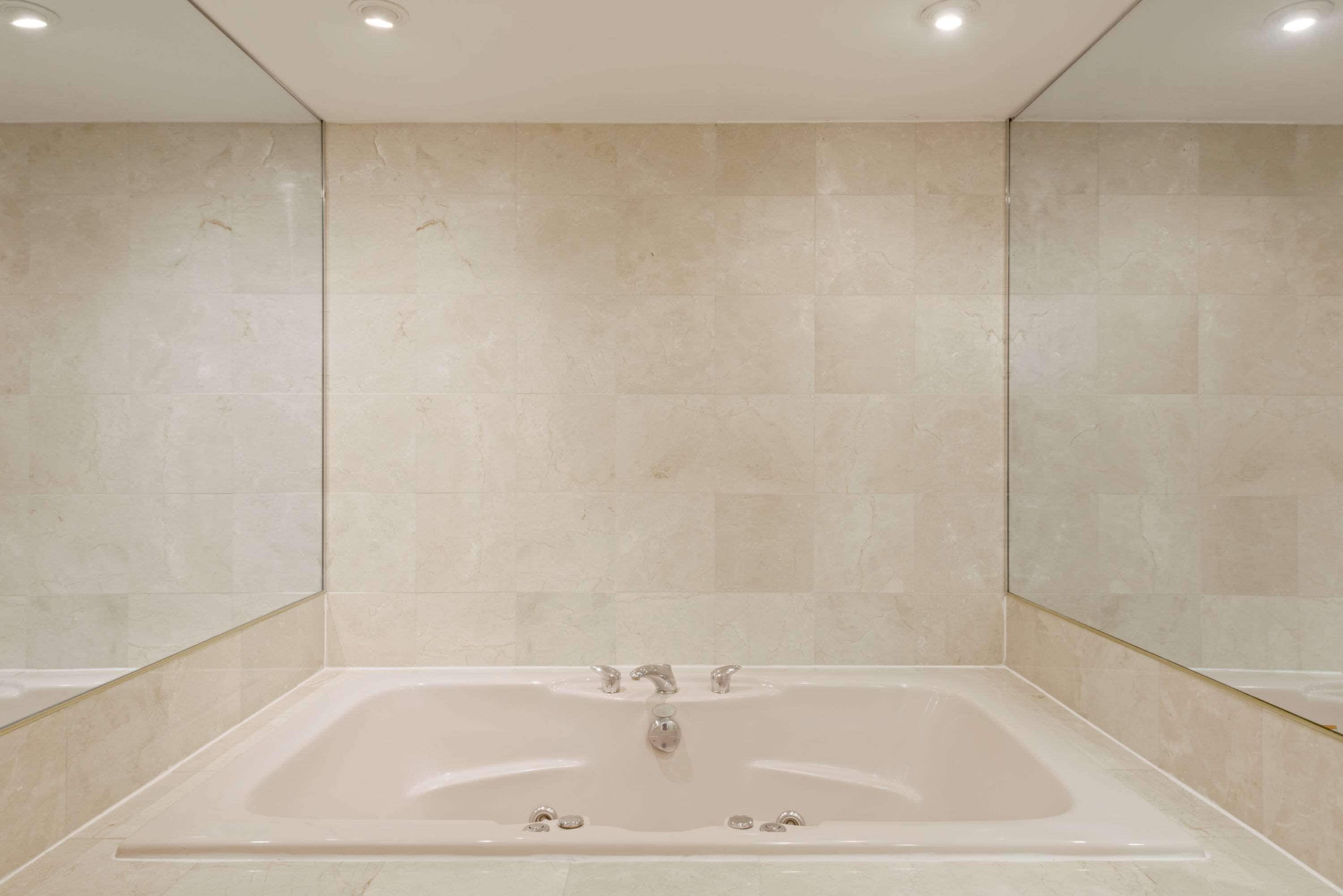 A modern bathroom with a large bathtub, tiled walls, and recessed ceiling lights.