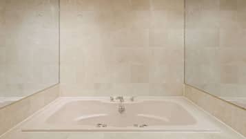 A modern bathroom with a large bathtub, tiled walls, and recessed ceiling lights.