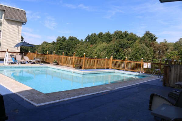 Una piscina rectangular con cerca de madera, sillas de descanso y vista a una ladera boscosa.