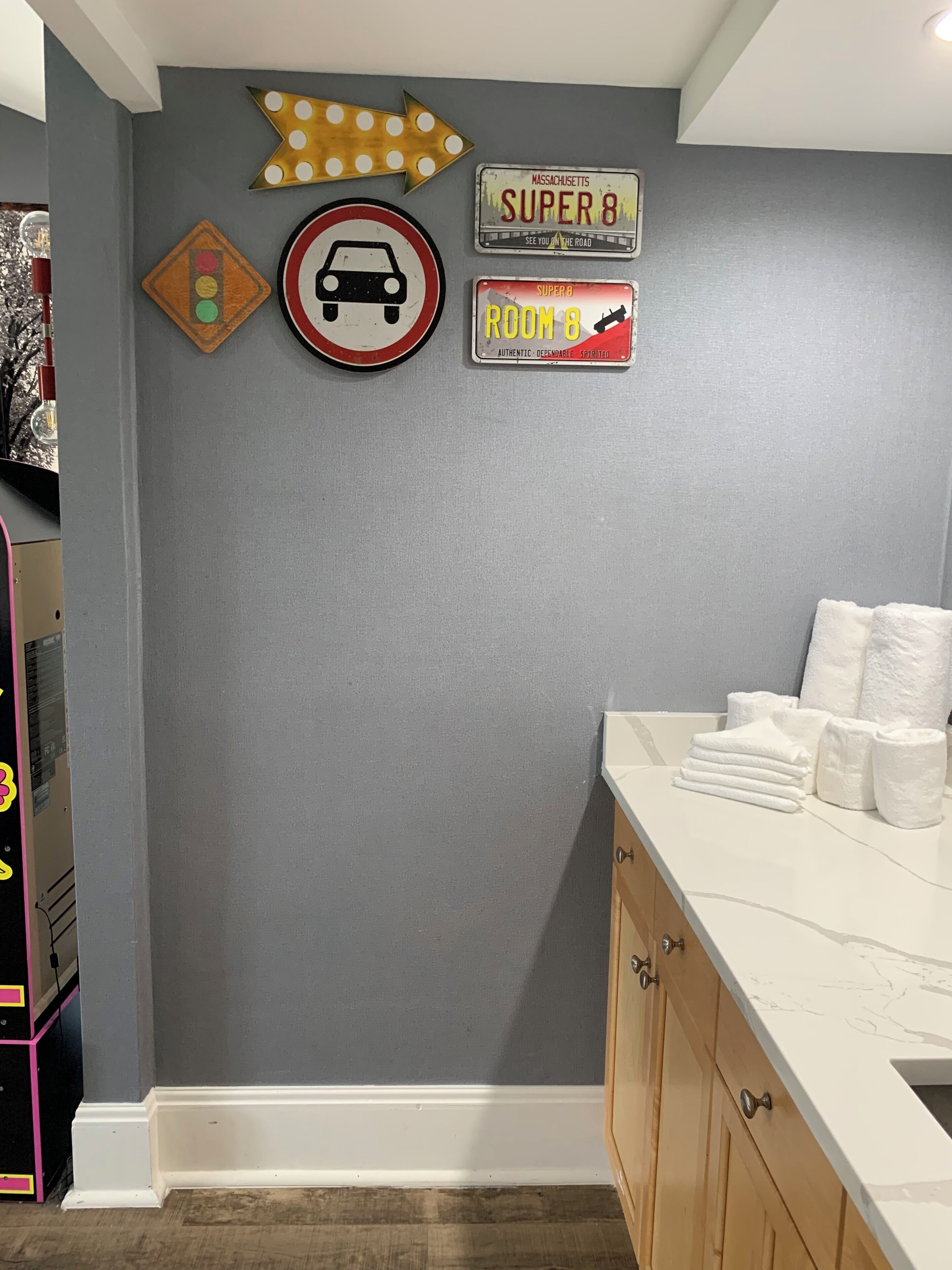 Un baño con lavamanos, toallas y adornos en la pared, incluyendo un letrero de 'no estacionar', una flecha direccional y un letrero de 'Massachusetts Super 8'.