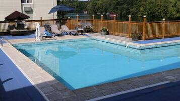 A rectangular swimming pool with a tiled edge, surrounded by a wooden deck with lounge chairs and a table.