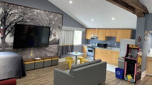 A modern living space with a kitchen, a sofa, a TV, and a children's arcade game. - Super 8 by Wyndham Sturbridge (Sturbridge)