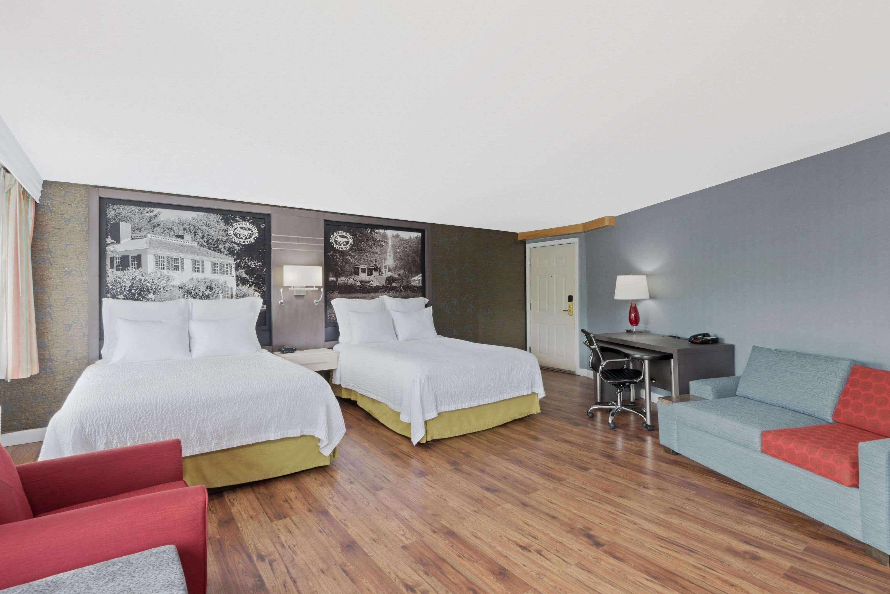 A hotel room with two beds, a desk, a chair, and a sofa.