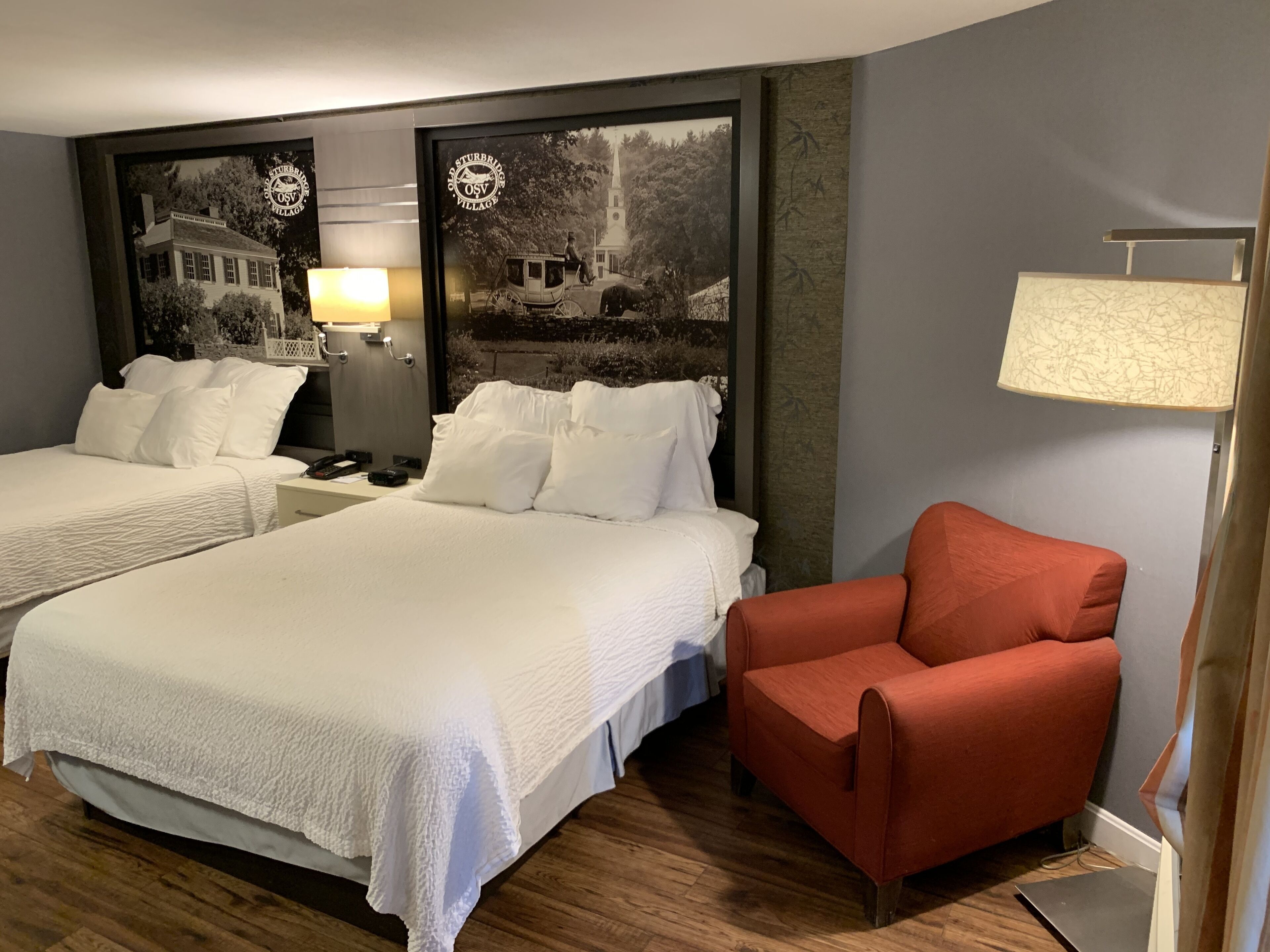 Una habitación de hotel con dos camas, un sillón rojo y una lámpara de pared.
