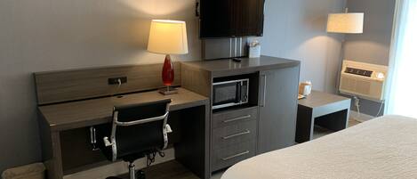 A hotel room with a bed, a desk with a chair, a TV, a microwave, and two lamps.
