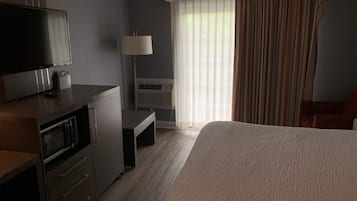 Habitación de hotel con cama, escritorio, televisión, aire acondicionado y ventana con cortinas.