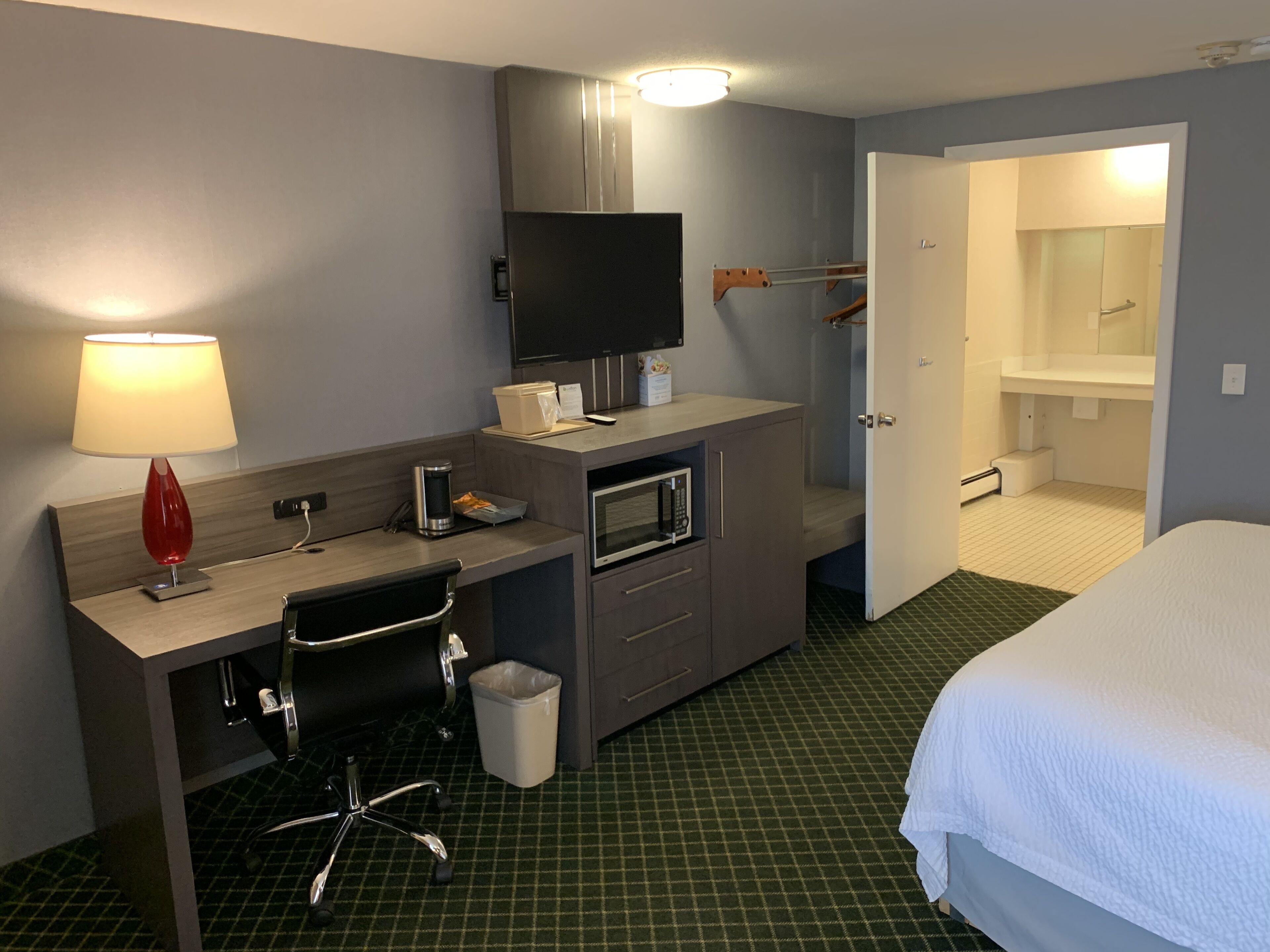 Habitación de hotel con escritorio, silla, televisión, microondas y cama.
