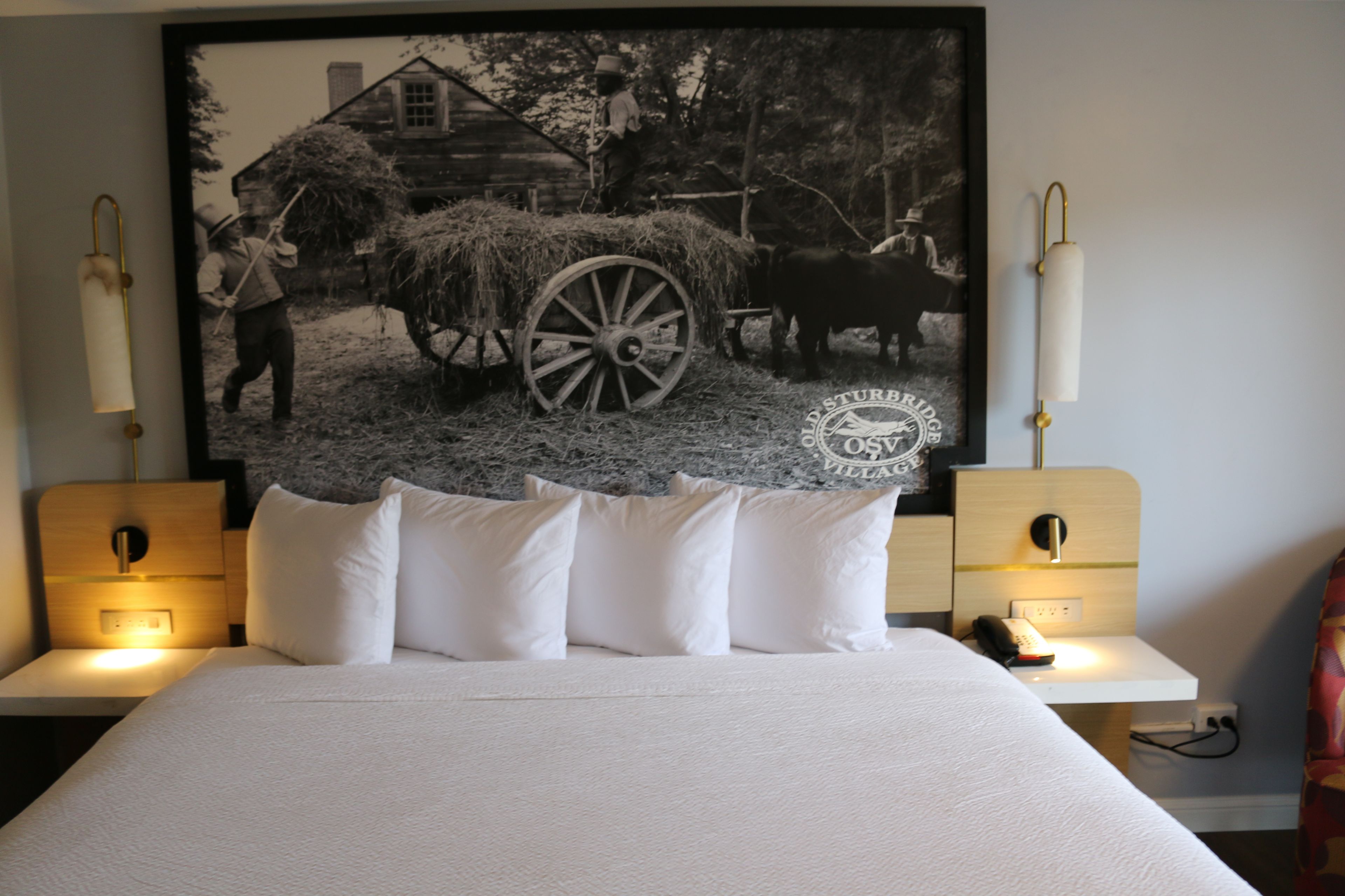 Une chambre à coucher avec un grand lit, deux tables de chevet et un tableau représentant une scène historique, accroché au mur.