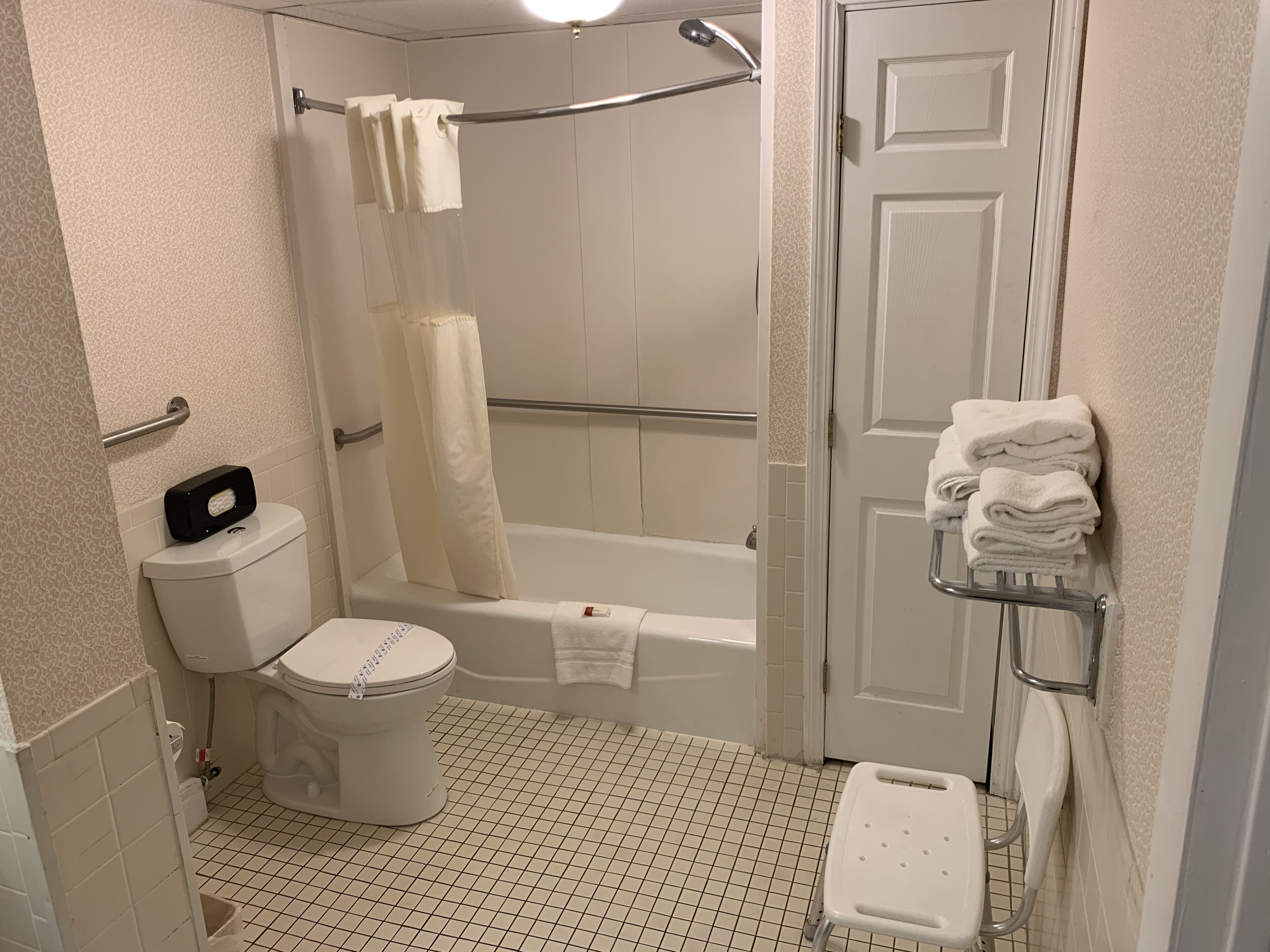 A bathroom with a toilet, a shower with a glass door, a bathtub, and a towel rack with folded towels.