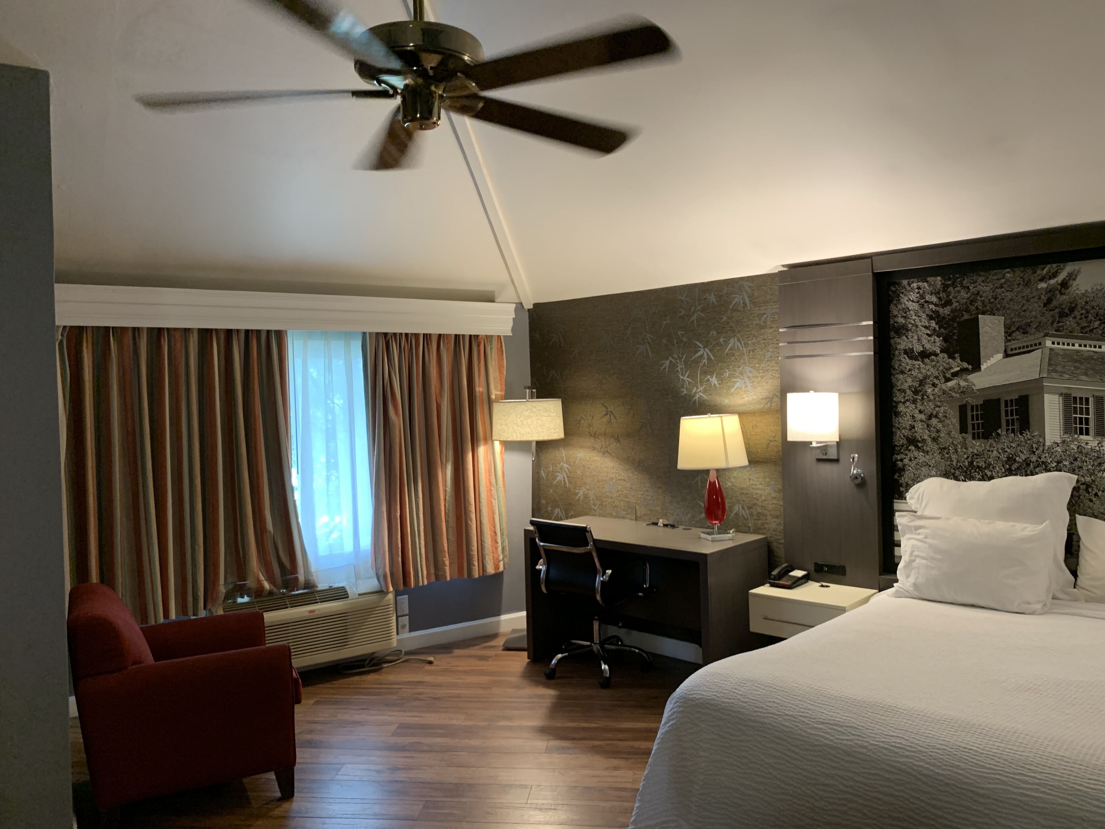 Una habitación de hotel con cama, escritorio, silla y ventilador de techo.