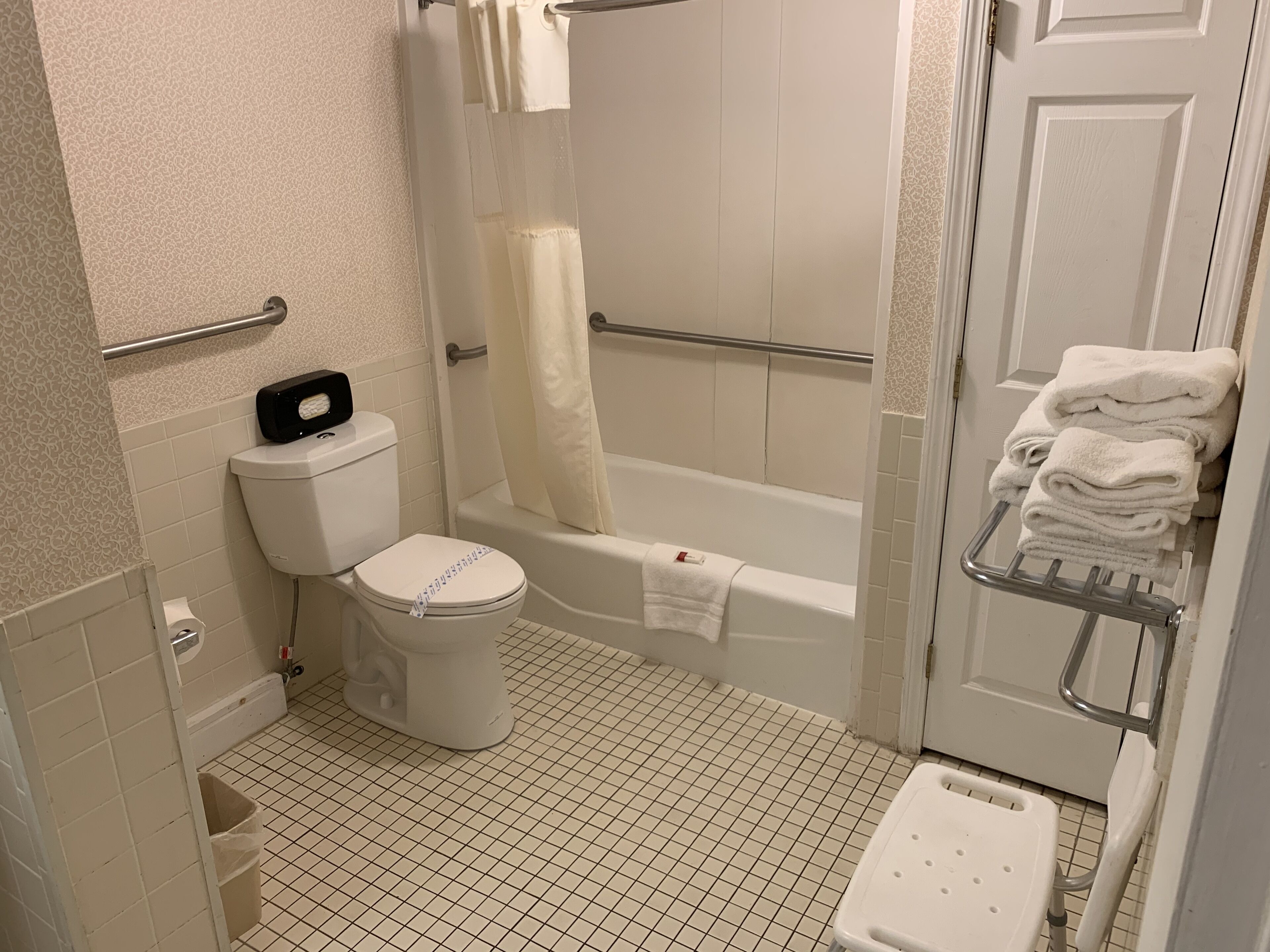 A bathroom with a toilet, bathtub, and a towel rack with folded towels.
