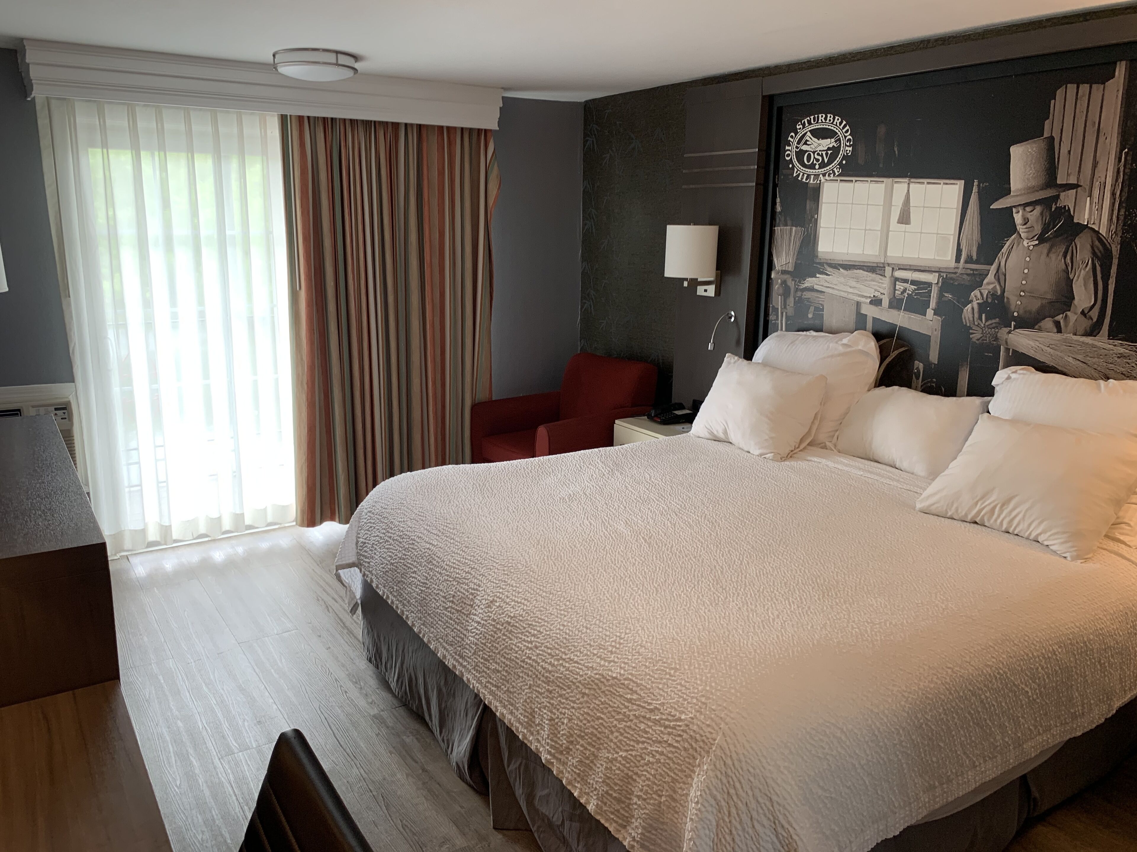A hotel room with a large bed, a desk, a chair, and a window with curtains.