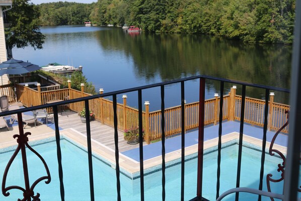 Una piscina con cubierta de madera y barandilla, con vistas a un lago con barcos.
