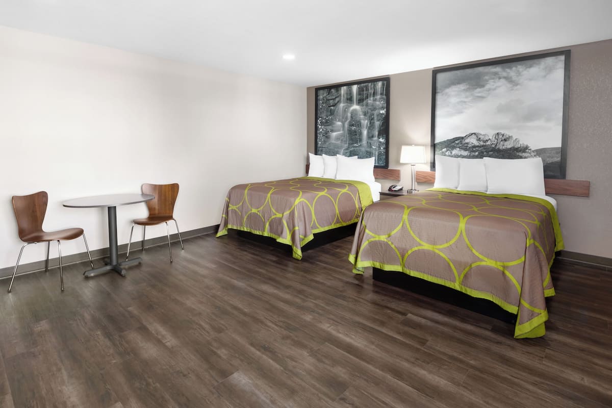 Una habitación de hotel con dos camas, una mesita pequeña y dos sillas.