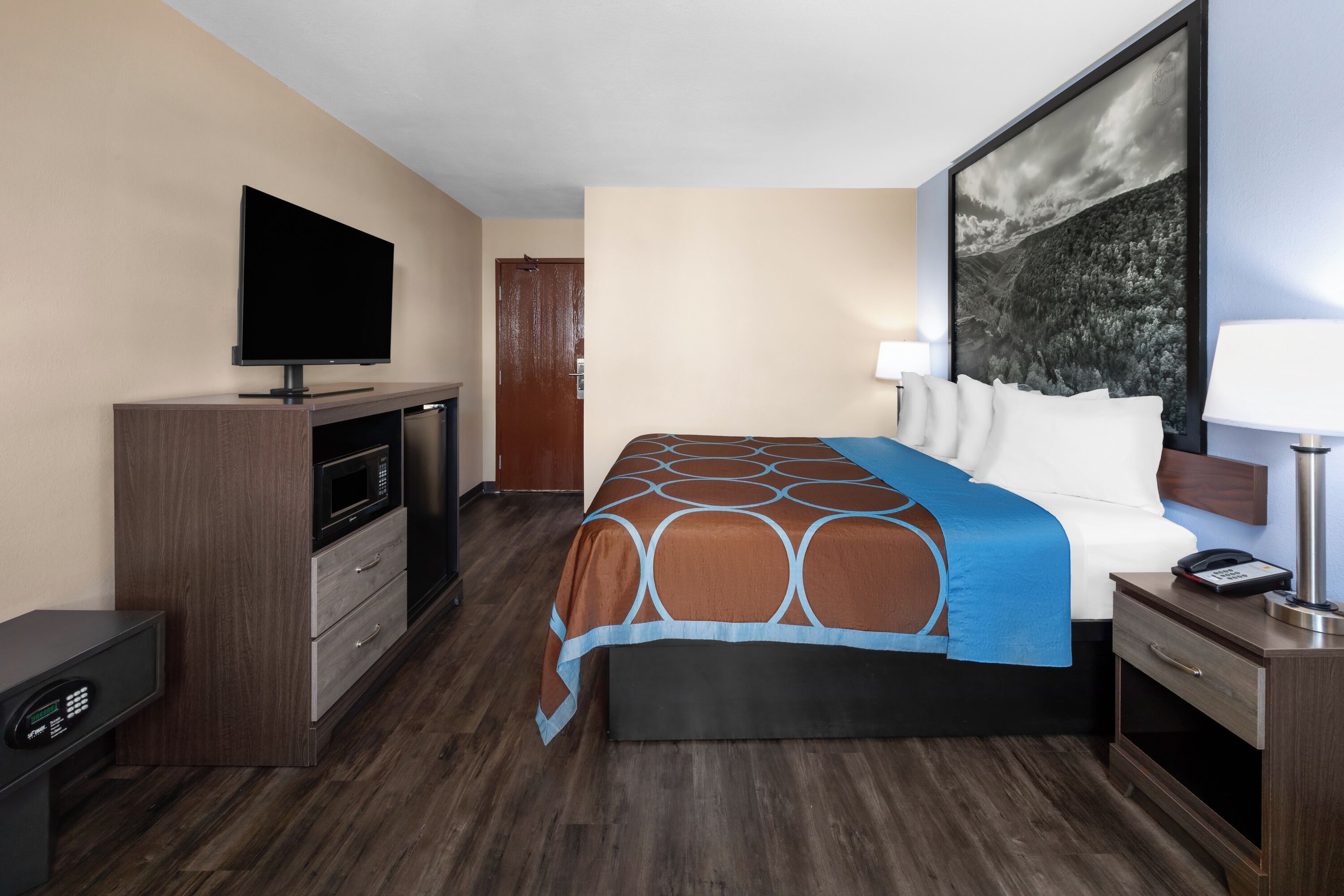 Habitación de hotel con una cama, un televisor de pantalla plana, un escritorio con ordenador, un microondas y una puerta que da a otra habitación.