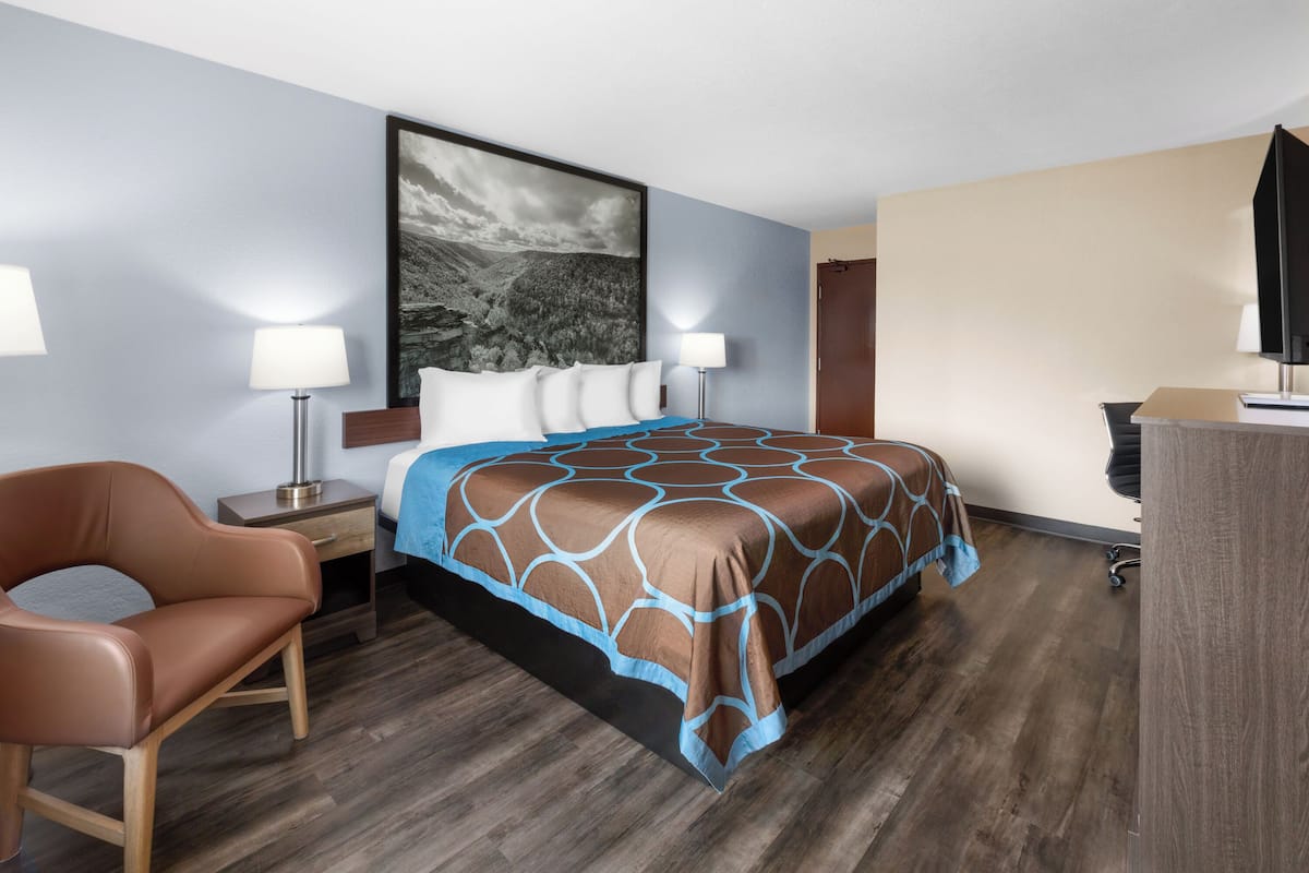 Habitación de hotel con cama, una silla, un escritorio y un cuadro grande en la pared.