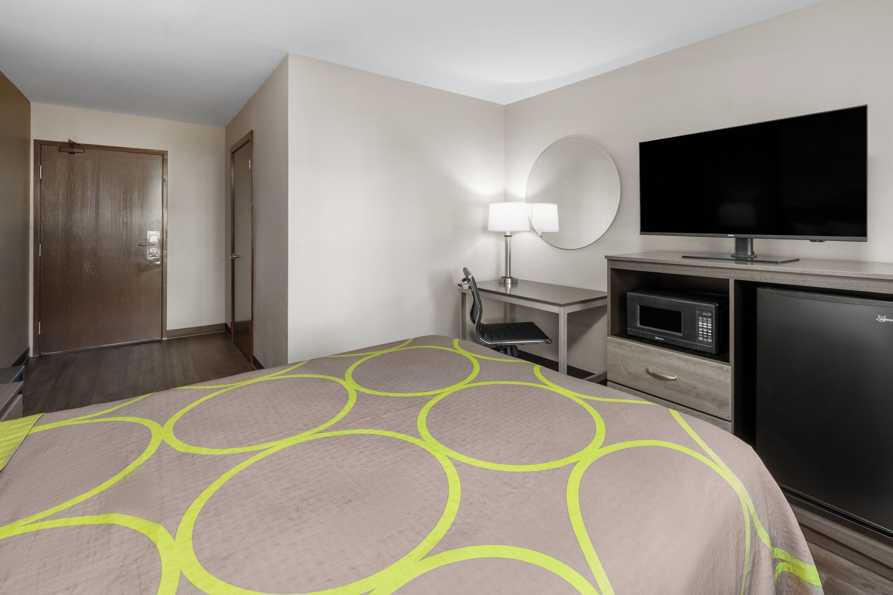 Habitación de hotel con cama, escritorio con lámpara, televisor, microondas y refrigerador.