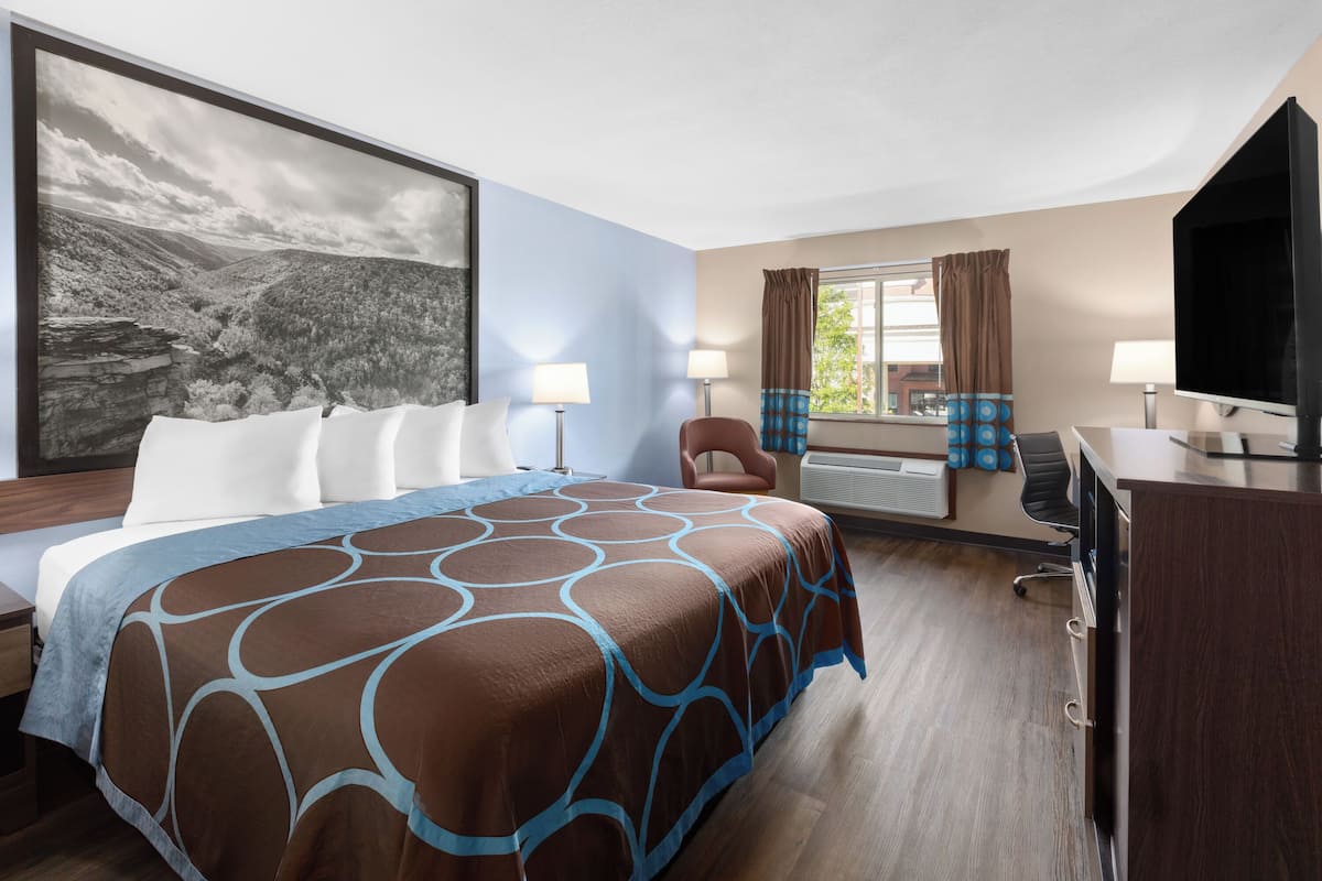 Una habitación de hotel con una cama grande, un escritorio, una silla, un televisor y una ventana con cortinas.
