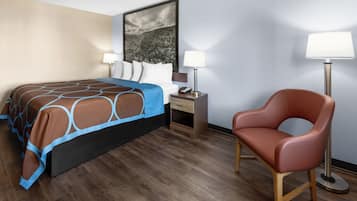 Una habitació d'hotel amb un llit, una taula de nit, una làmpada, una cadira i un quadre a la paret.