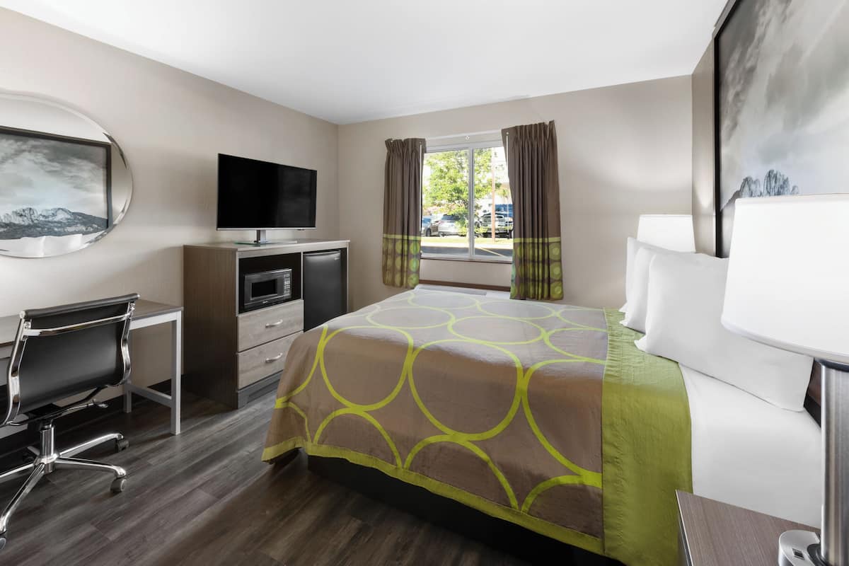 Habitación de hotel con cama, escritorio, silla, televisor y ventana con cortinas.