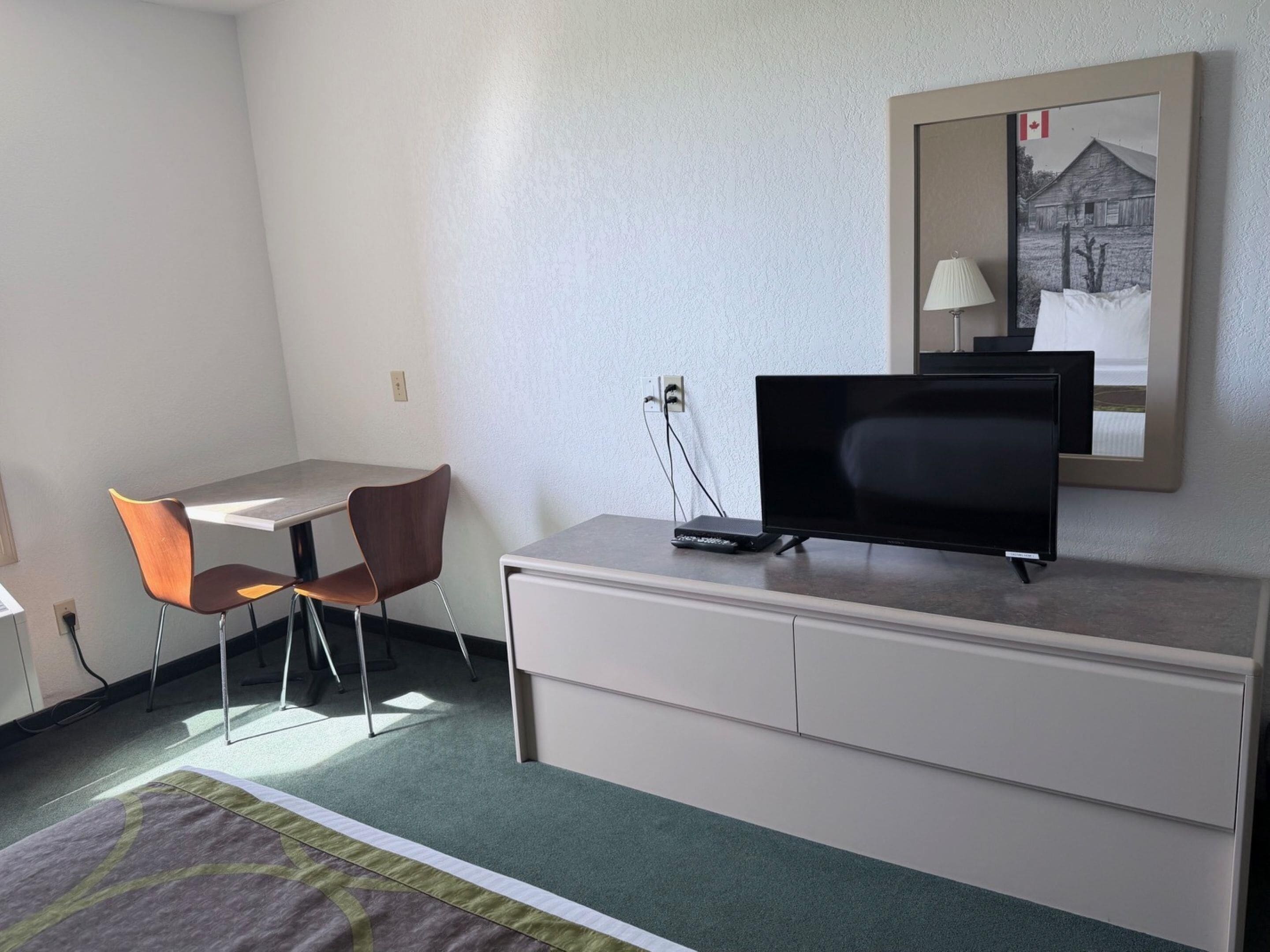 Una habitación de hotel con escritorio, dos sillas, televisor, cómoda y espejo.