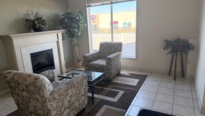 A living room with a fireplace, two patterned armchairs, a glass coffee table, and a potted plant.