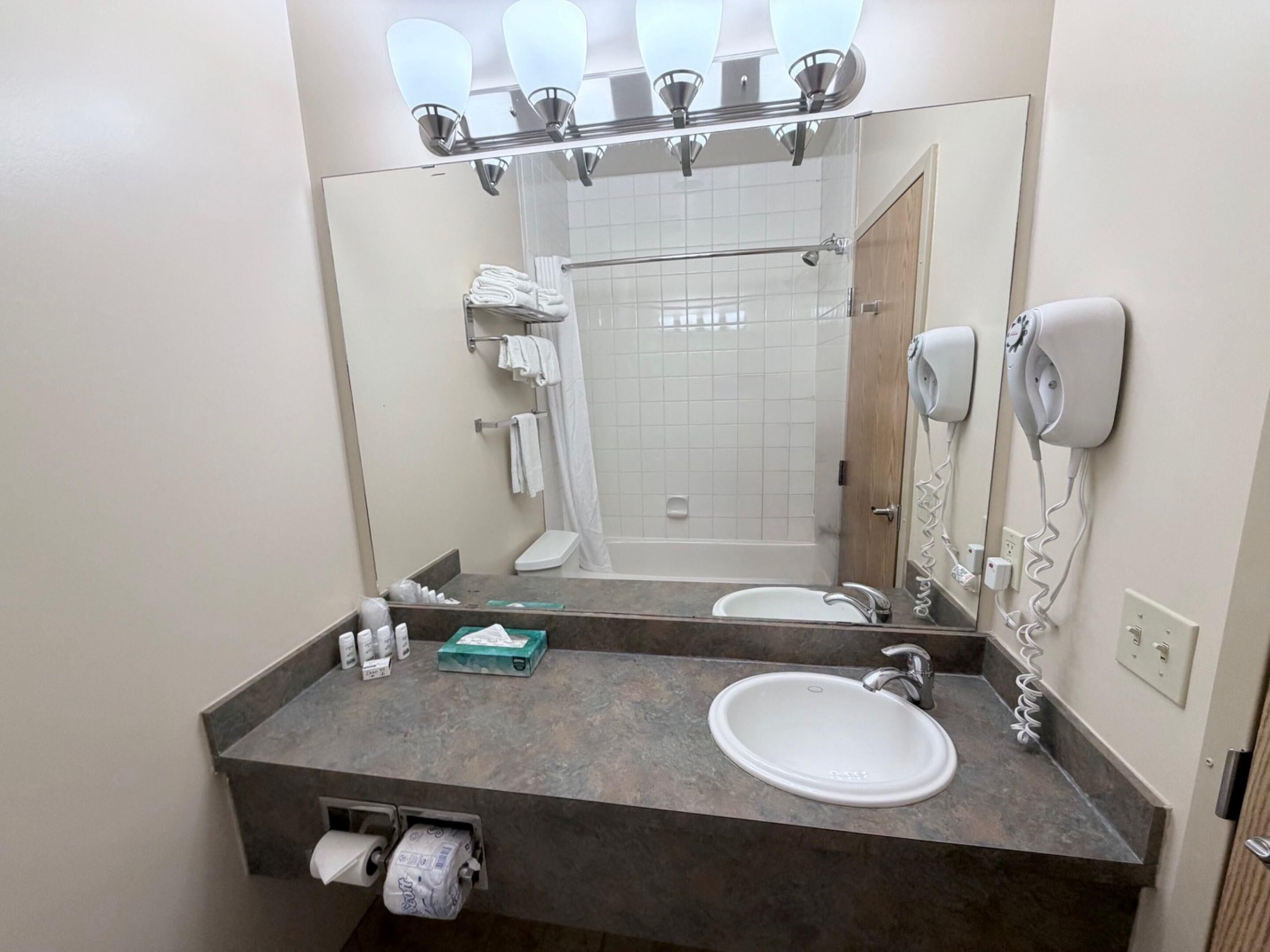 Un baño con lavamanos, espejo, toallero, ducha y secador de pelo.