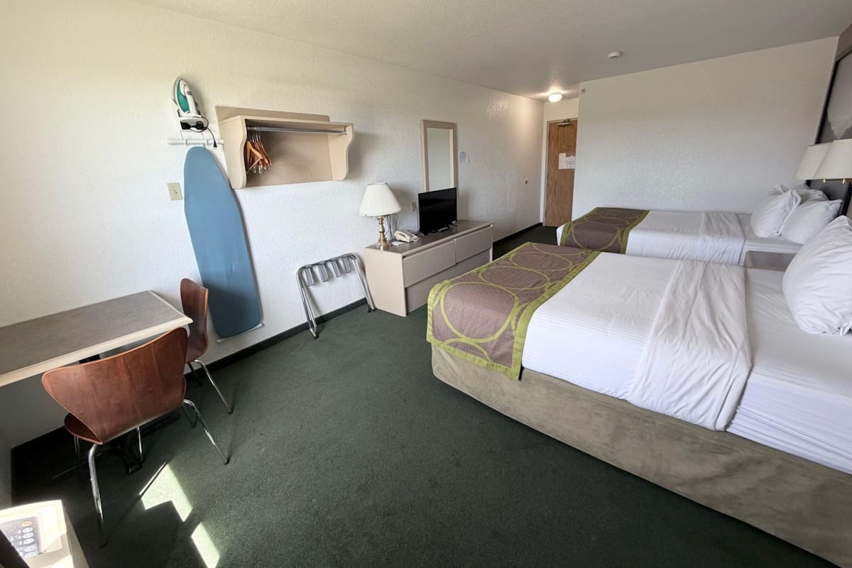Une chambre d’hôtel équipée d’un bureau, d’une chaise, de deux lits, d’une télévision et d’une planche de surf.