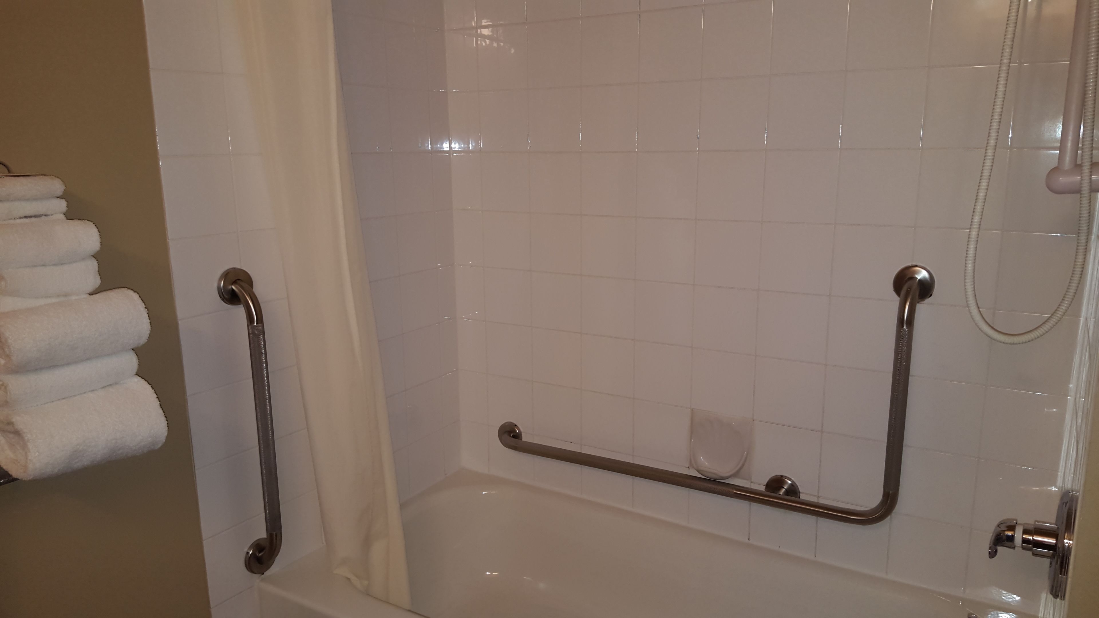 A bathroom with a bathtub, grab bars, a showerhead, and a towel rack.