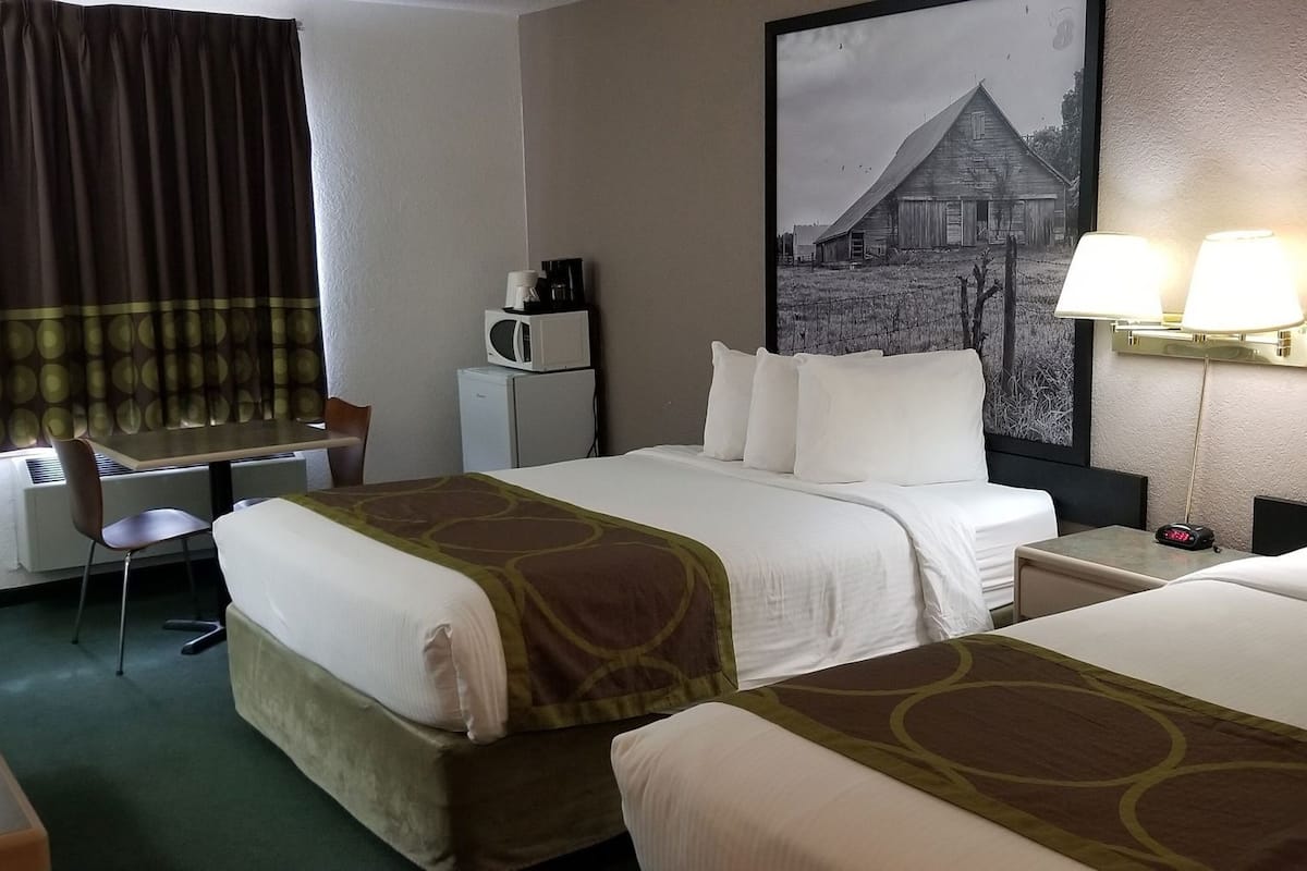 Une chambre d’hôtel avec deux lits, un bureau, une chaise, une machine à café, une horloge et des tableaux encadrés aux murs.
