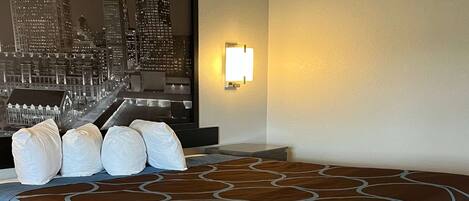 A hotel room with a large bed, a cityscape wall art, and a nightstand with a lamp.