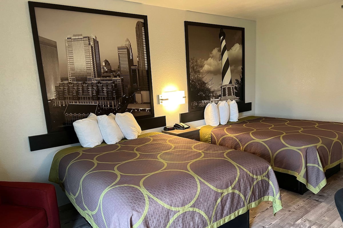 A hotel room with two beds, a cityscape view, a nightstand with a lamp, and a red chair.