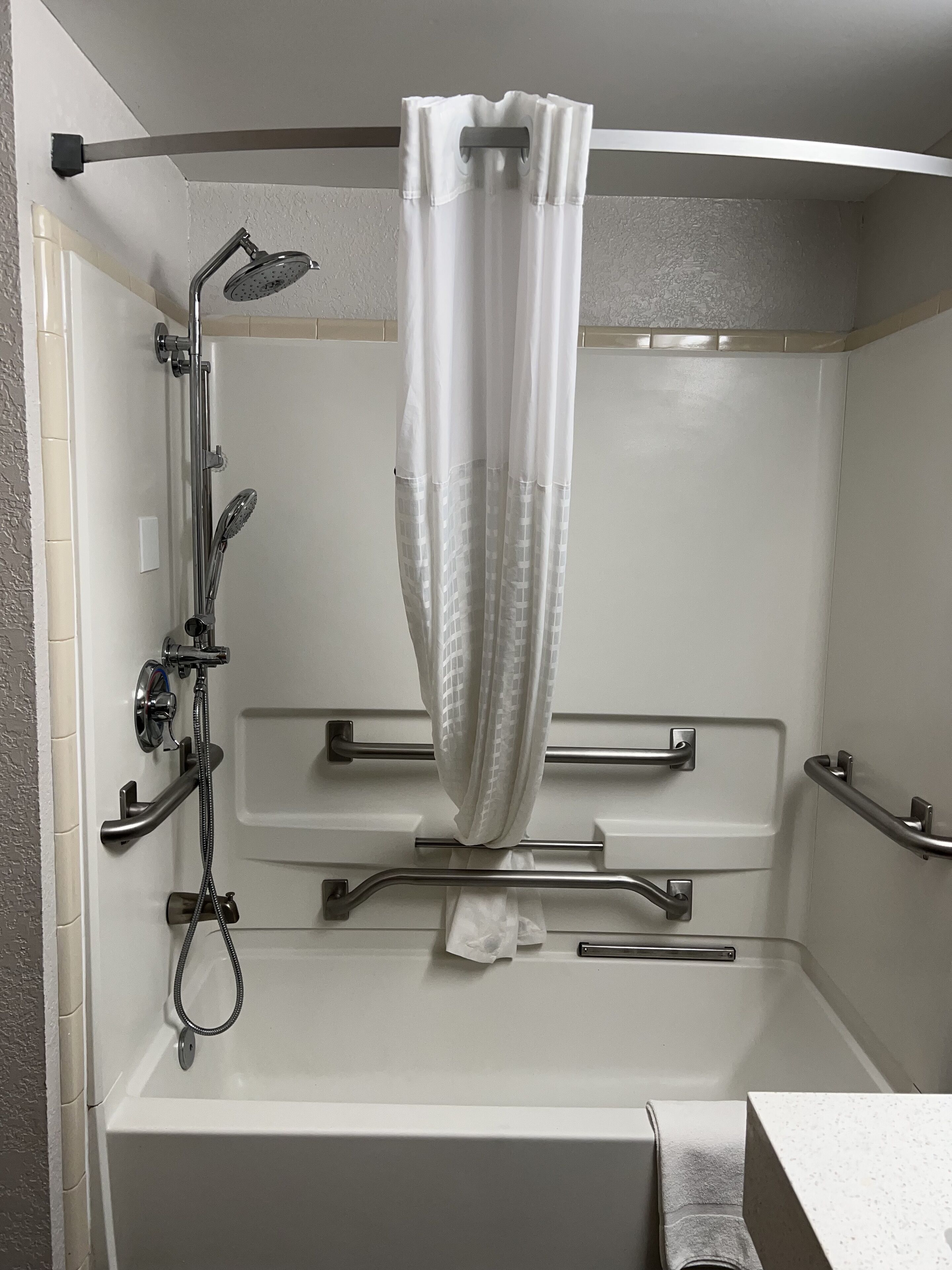 A shower area with a handheld showerhead, a handheld shower head, a grab bar, and a towel rack.